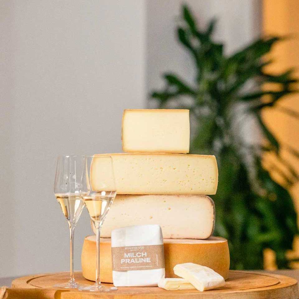 Zwei Gläser Champagner stehen neben einem Käseturm und einem Käse der Münchner Käse Manufaktur