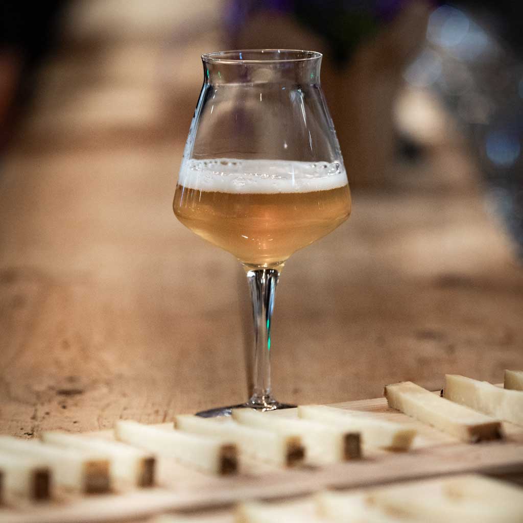 Volles Tasting-Bierglas vor schoen geschnittenem Hartkaese