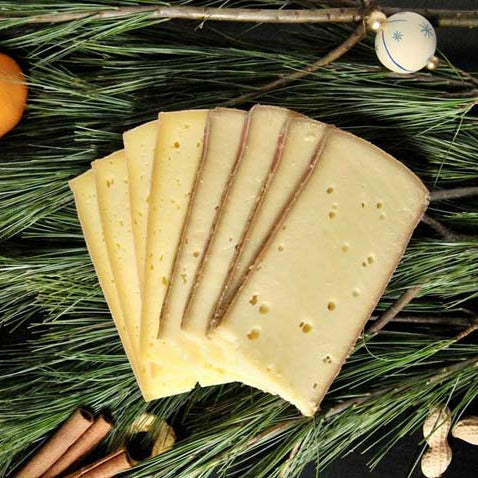 Aufgeschnittene Scheiben Raclette auf Tannennadeln.