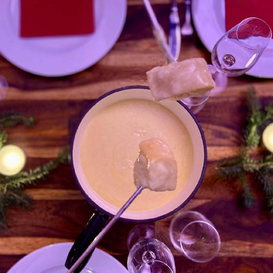 zwei Brote auf Gabeln mit Fondue über einem Fonduetopf