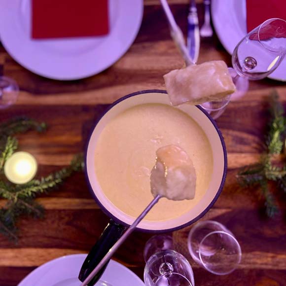 Eine Fonduegabel mit einem Stück Brot über einem Fonduekessel