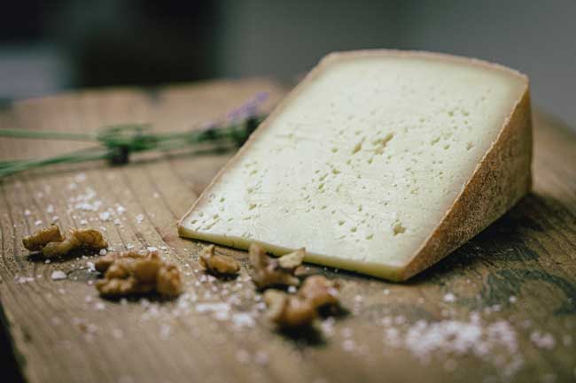 Zu sehen ist der Gspusi der Käse der Münchner Käse Manufaktur. Er liegt auf einem Holzbrett und ist angeschnitten.