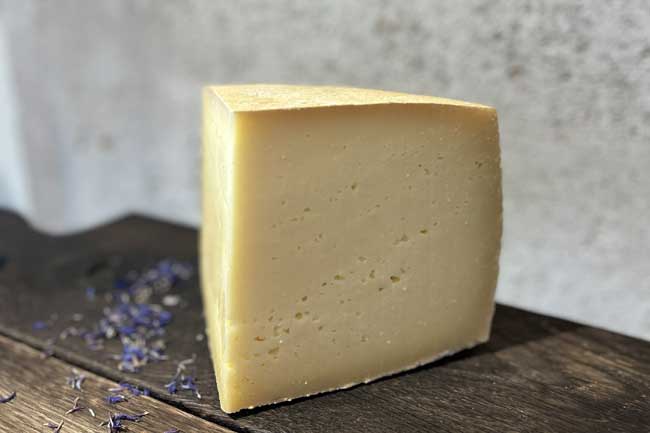 Zu sehen ist der hartl der Münchner Käse Manufaktur. Er liegt auf einem Holzbrett und ist angeschnitten. Es ist ein Hartkäse aus München.