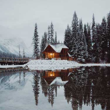 Eine verschneite Hütte vor einem See.
