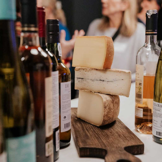 Kaese liegen aufgestapelt auf einem Tisch mit Weinflaschen beim Tasting