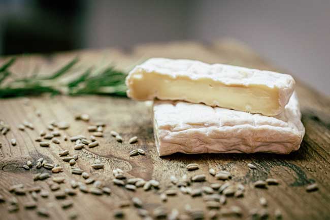 Zu sehen ist die Milchpraline der Käse der Münchner Käse Manufaktur. Er liegt auf einem Holzbrett und ist angeschnitten.