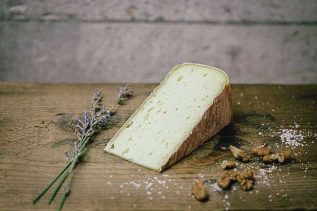 Zu sehen ist der Münchner Mutschli der Käse der Münchner Käse Manufaktur. Er liegt auf einem Holzbrett und ist angeschnitten. Es ist ein Schnittkäse.
