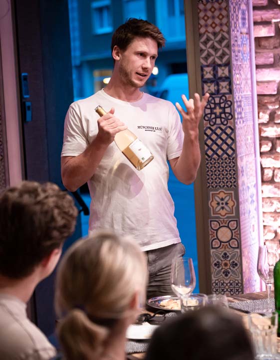 Sebastian von der Münchner Käse Manufaktur präsentiert bei einem Käse und Wein Tasting einen Wein.