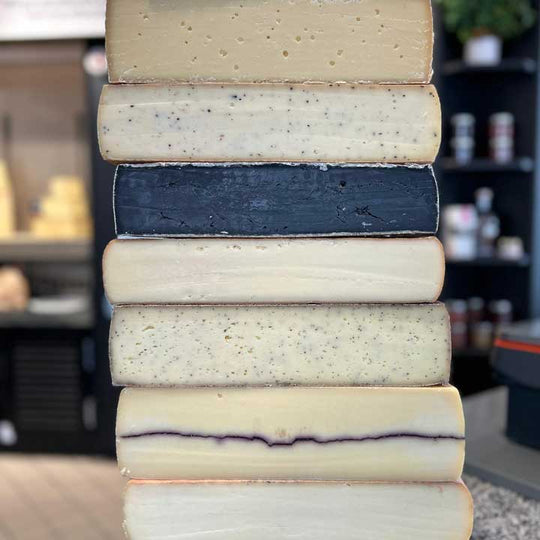 Zu sehen ist ein Turm aus Raclette Laiben. Darunter einige außergewöhnliche wie schwarzes Raclette oder Raclette mit Erdbeersamen.